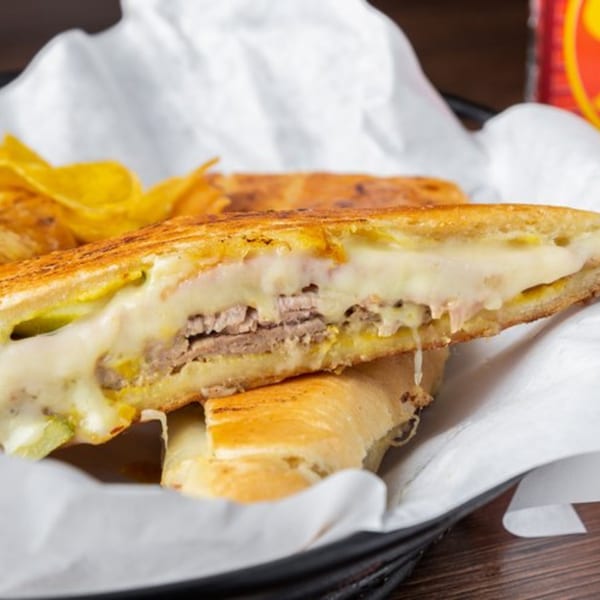 A Cuban sandwich from Havana Grill, cut in half, revealing melted cheese, pork, and pickles, with plantain chips.