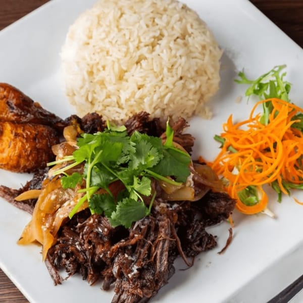Cuban shredded beef with rice, plantains, and a side salad on a white plate.