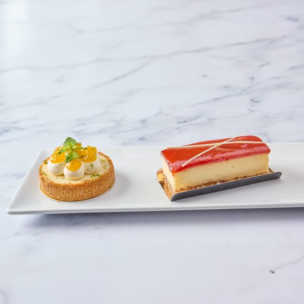 Two Cuban desserts, a key lime tart and a guava cheesecake, on a white rectangular plate.