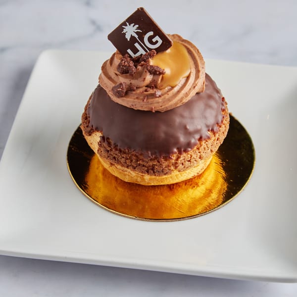 A chocolate cream puff with caramel drizzle and a Havana Grill logo chocolate square on a white plate.