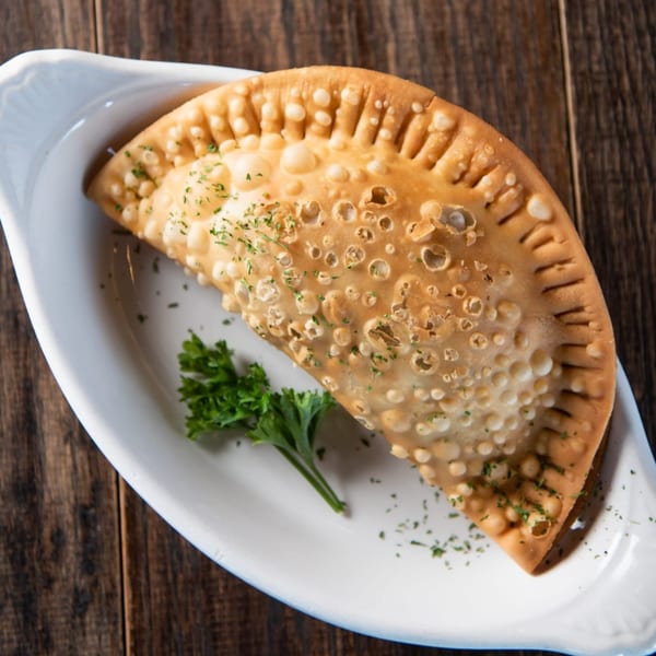 Golden-brown Cuban empanada with crimped edges and parsley garnish on a white dish.