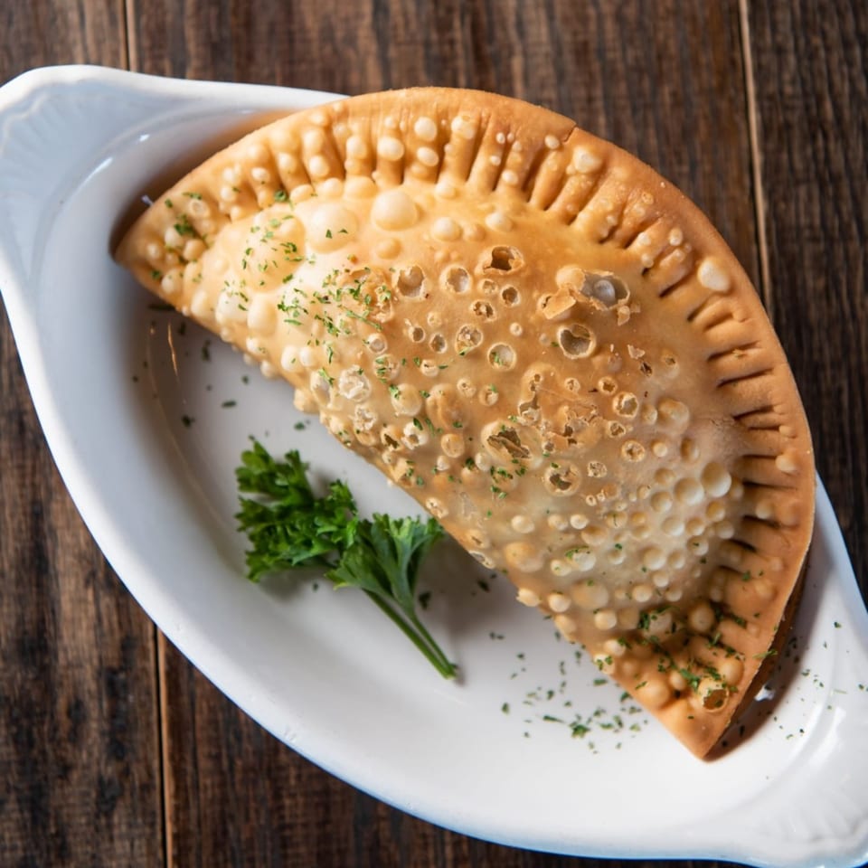 Golden-brown Cuban empanada with crimped edges and parsley garnish on a white dish.