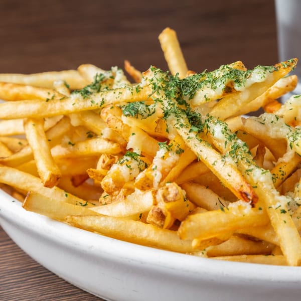 Close-up of golden french fries topped with melted cheese and green herbs in a white bowl.