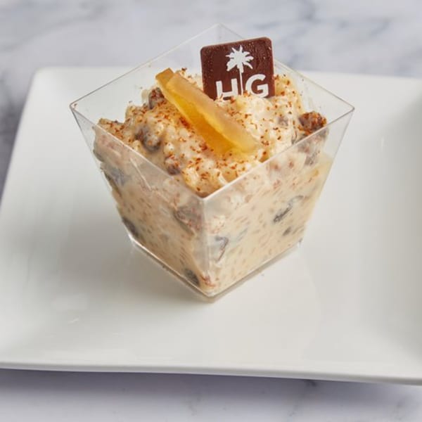 Cuban rice pudding dessert in a clear square cup, garnished with candied fruit and a chocolate logo.